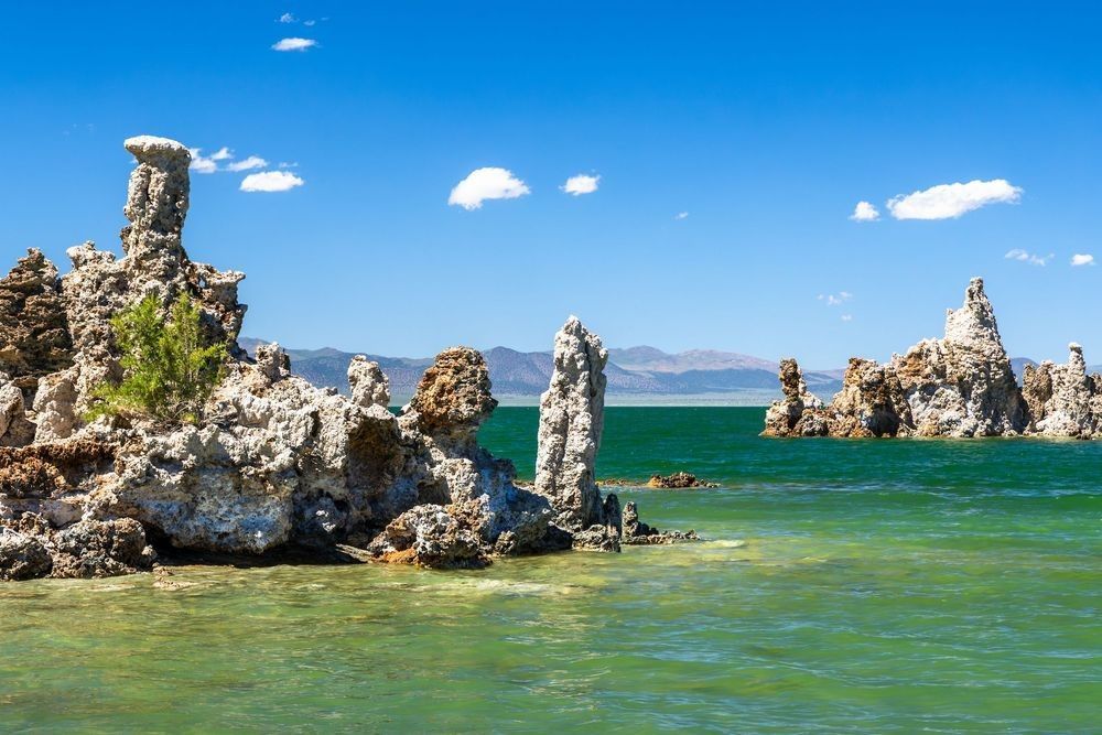 "Tufas at Mono Lake 16" - Dramatic tufa towers rise from the aqua-green waters of Mono Lake at the South Tufa area near Lee Vining, California, in the Eastern Sierra. These striking calcium carbonate formations stand against distant mountains and a vivid blue sky dotted with clouds, one of California's most iconic and otherworldly natural landscapes.