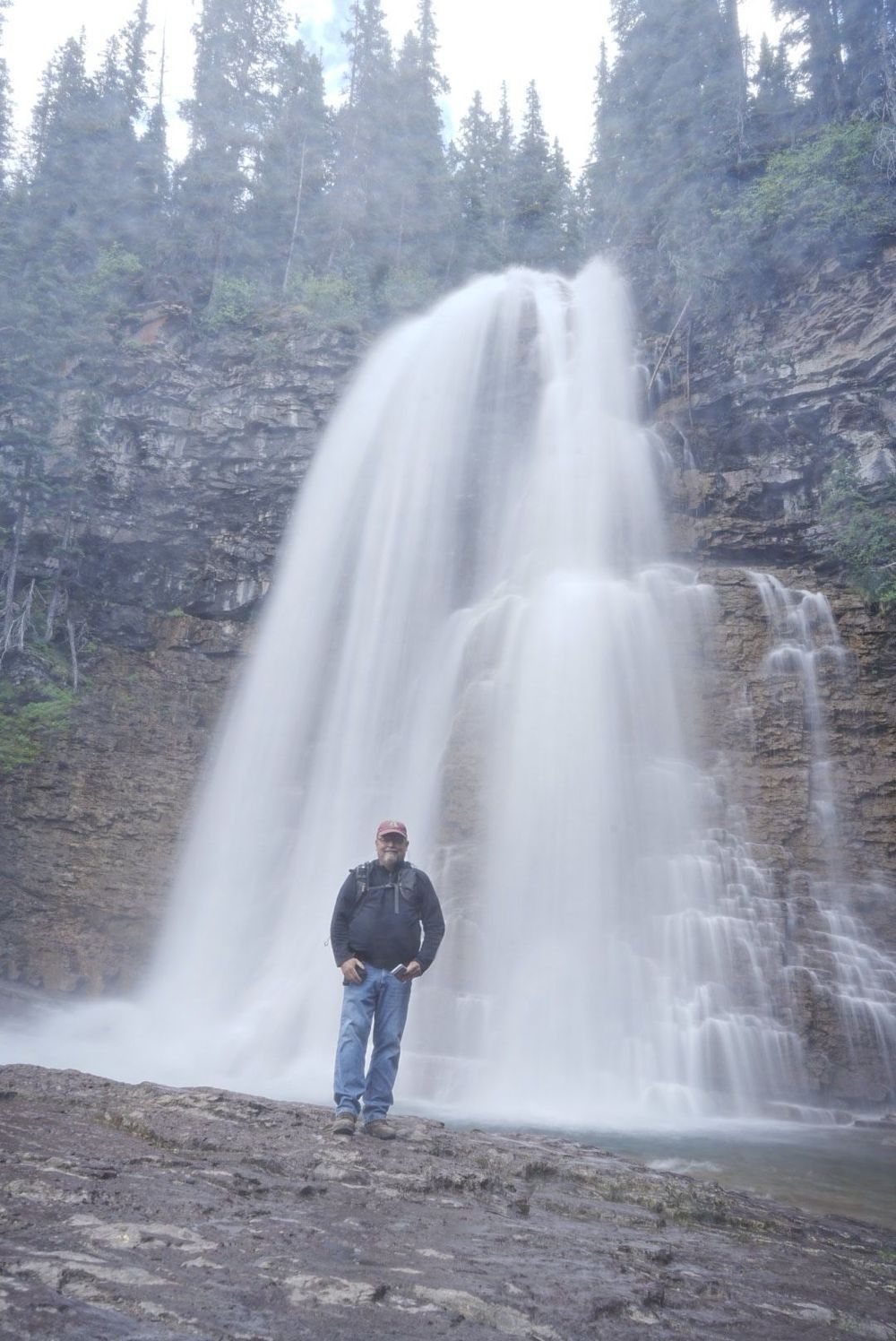 Photographer standing beside the upper cascades of Virginia Falls, showing the immense scale of Glacier National Park.