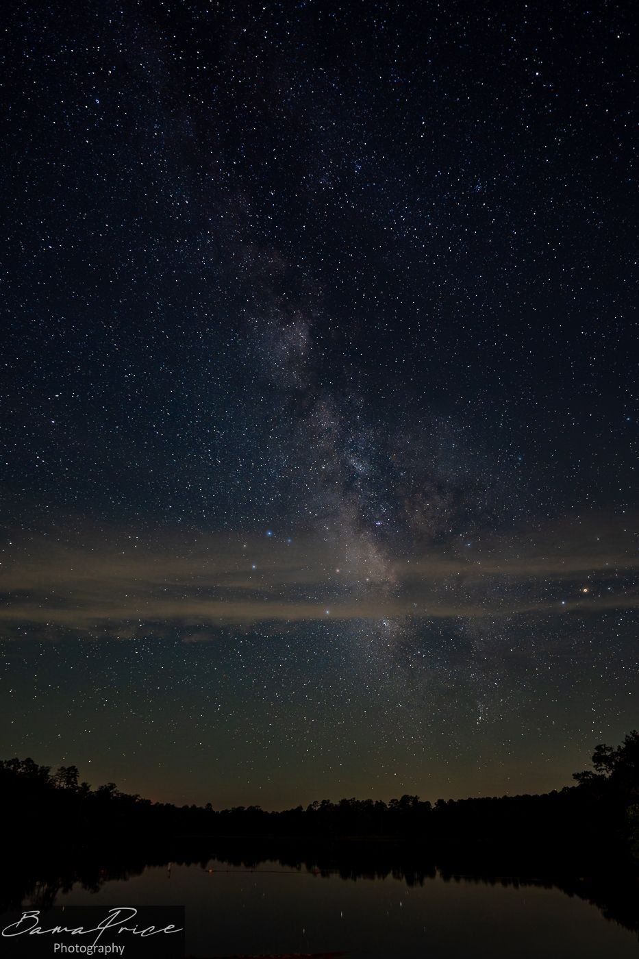 ilky Way rising above silhouetted trees at Payne Lake, Alabama, with a narrow band of clouds crossing the star-filled night sky.