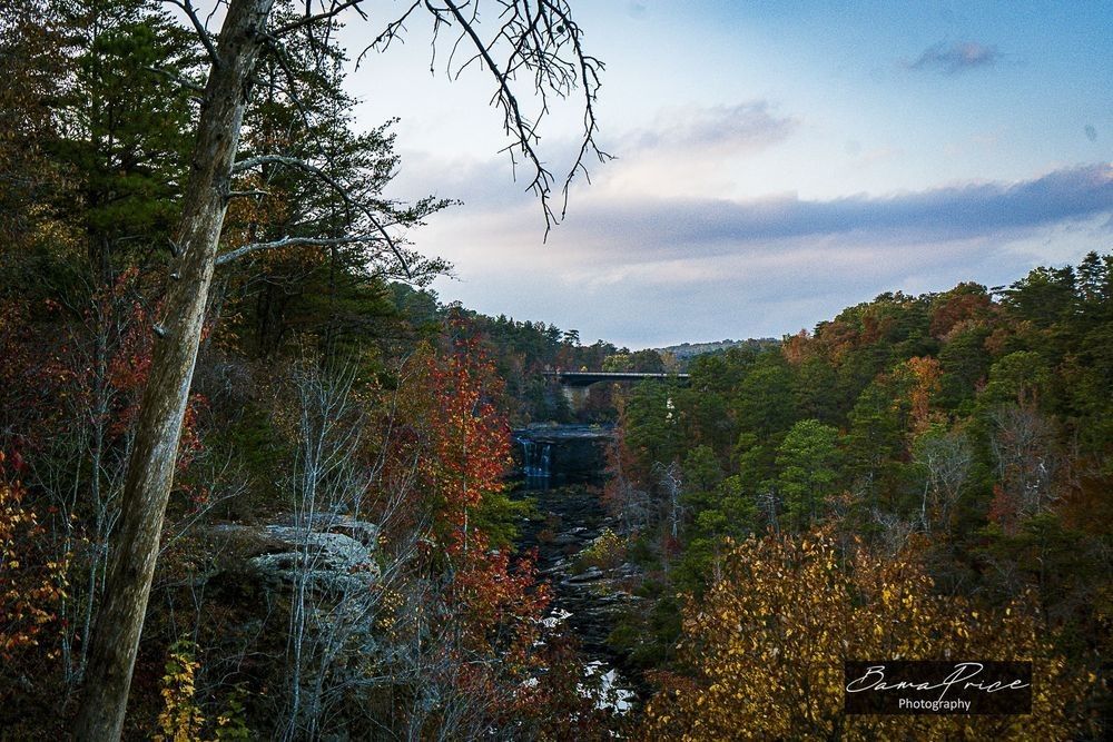 Little River Falls surrounded by vibrant orange, red, yellow and green autumn foliage in Little River Canyon, Alabama, beneath a softly illuminated evening sky.