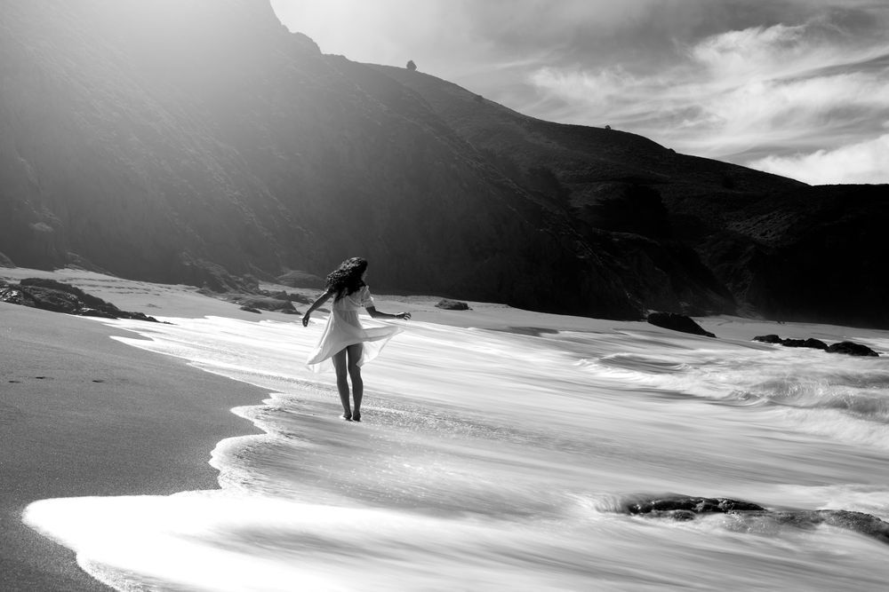 Depiction of a woman walking along the beach with flowing water and clouds