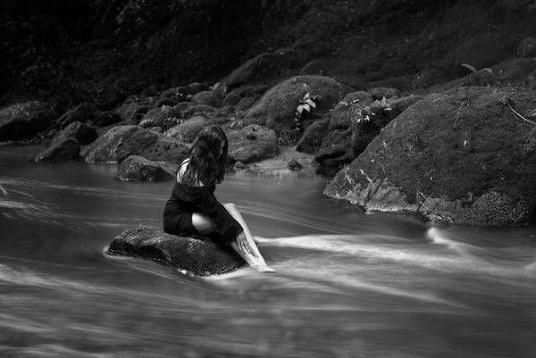 A black and white long exposure portrait of a woman with water flowing around her