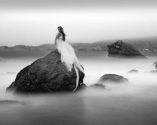 A black and white portrait of a woman sitting on a rock
