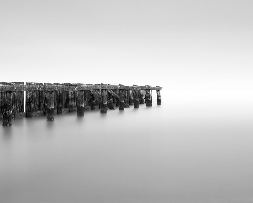 A long exposure black and white photograph of a dock