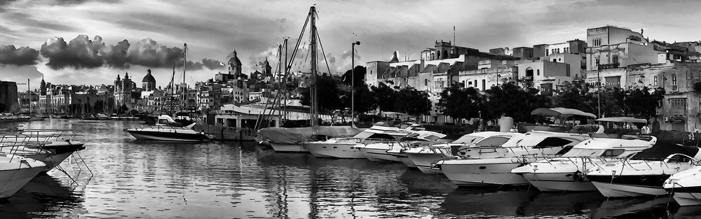 Black-and-white panoramic view of a malta harbor with yachts and historic waterfront buildings