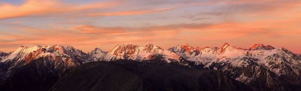 Snow-covered Colorado Gore Mountain Range illuminated by warm sunset light beneath a colorful sky.