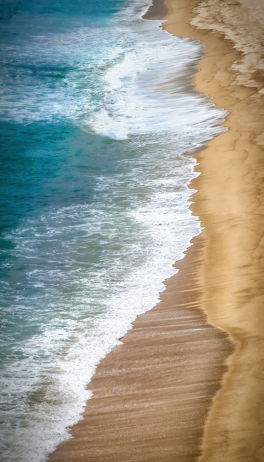Vertical aerial view of turquoise waves meeting a sandy shoreline, illustrating a tall fine-art print for a narrow wall space.