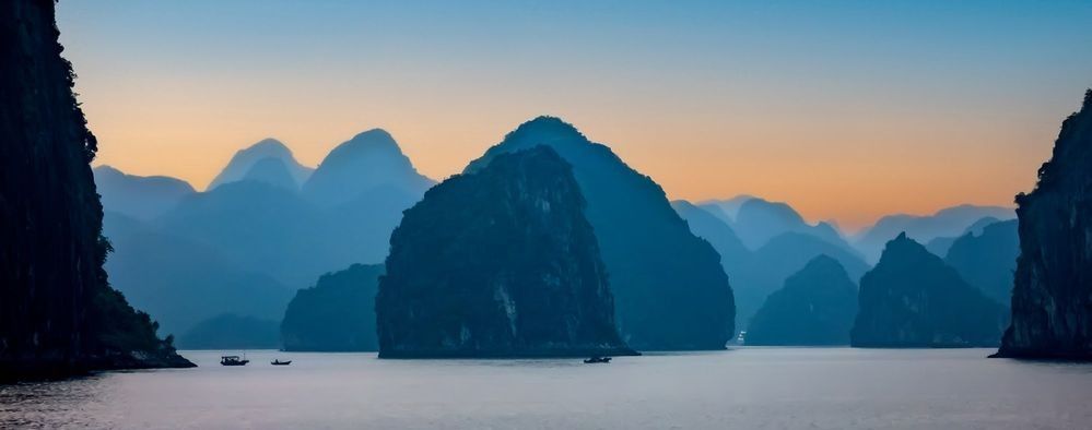 Blue-hour view of limestone karsts rising from calm water in Ha Long Bay, Vietnam.