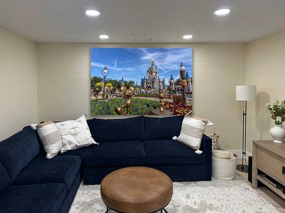 Golden Mickey and Minnie statues pose before Cinderella Castle with fall decor, Magic Kingdom print on a living room wall above a sofa.