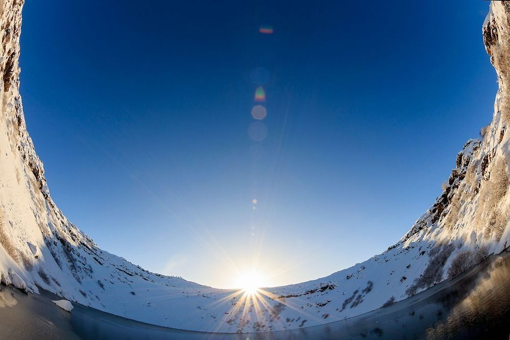 Snow-covered volcanic caldera landscape in Iceland with sunrise, crater walls, blue sky, and volcanic terrain