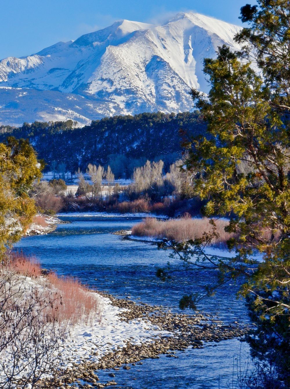Snow-fed river winding through a mountain valley, showing flowing water, riparian habitat, and the connection between snowpack, river systems, and landscape hydrology