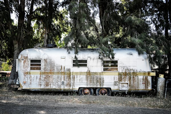 A retired travel trailer sits peacefully beneath a tree windbreak of trees at the Good Humus Produce farm.