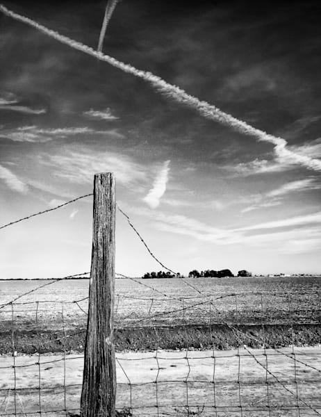 Jet trails and barbed wire criss-cross over a farm field in Yolo County, California.