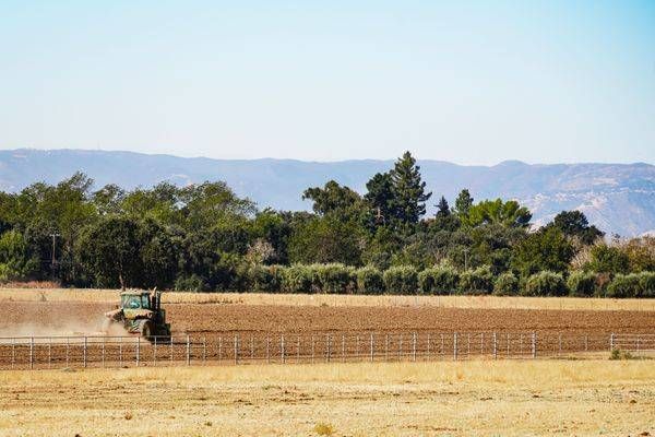 A tractor in the distance drags a harrow to prepare a field for new planting as the Coastal Range sits on the Northern California horizon.