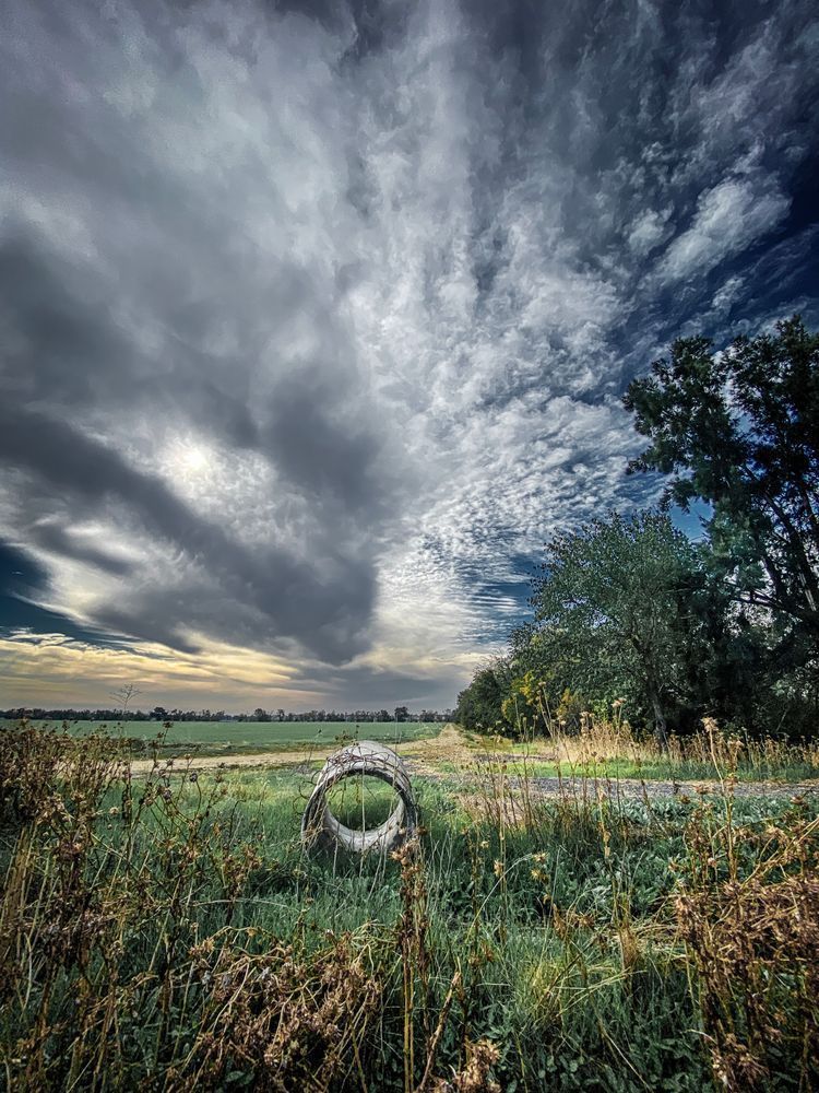 Springtime storm clouds float above a farm field as late afternoon sunlight streams through them.