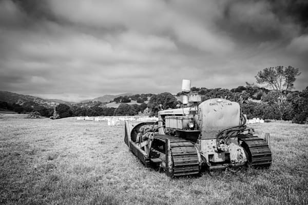 Heavy road-making equipment stands by to keep rolling farmland accessible to farmers and cattle alike.