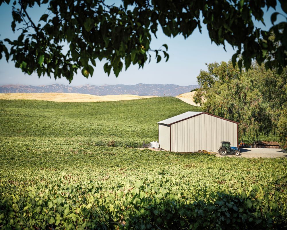 A tractor stands ready next to an equipment shed, framed by oak leaves.
