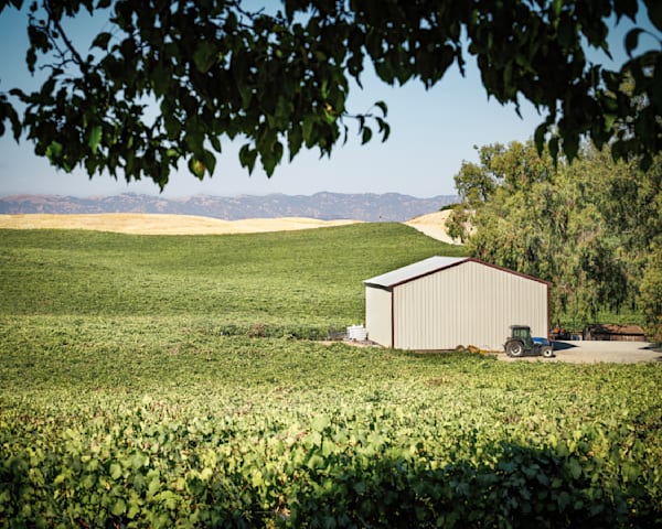 A tractor stands ready next to an equipment shed, framed by oak leaves.