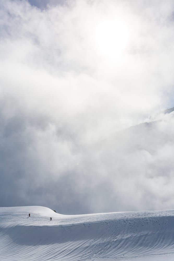 Two tiny human figures descending a snow covered ridge as the sun breaks through the rising clouds, Mount Rainier National Park, Washington, USA.