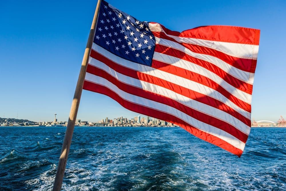 An American flag waving in the wind behind a boat on the Puget sound with downtown Seattle, WA in the background, USA.