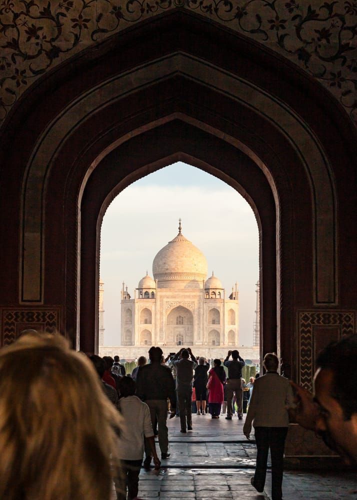 Looking through the main entrance gate at The Taj Mahal in Agra, India with tourists taking pictures in the foreground.