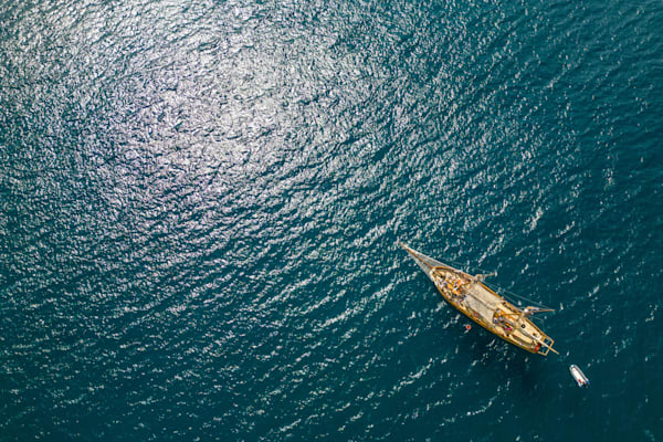 Following the Light - Aerial view of a sailboat crossing sun reflections on the sea