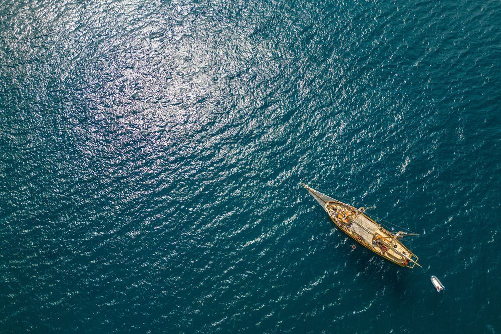 Following the Light - Aerial view of a sailboat crossing sun reflections on the sea