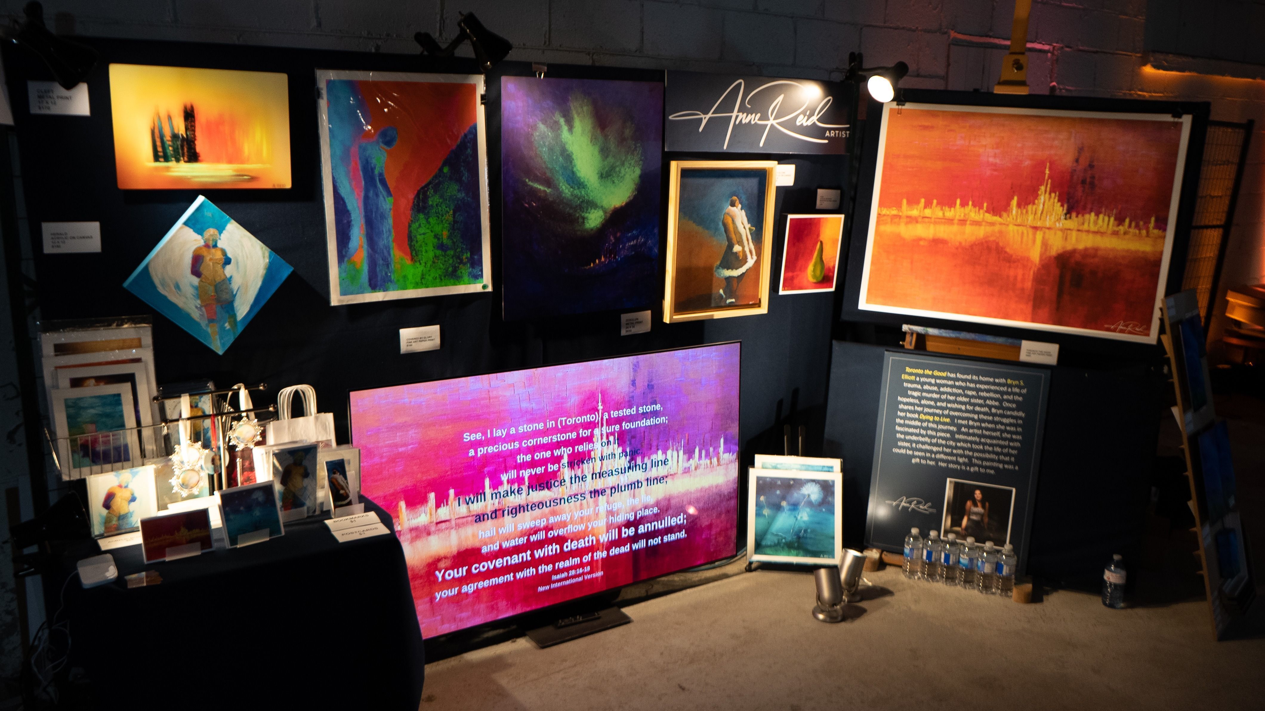 Anne Reid Artist booth at RAW Toronto showing metal prints and a large Samsung screen displaying artwork and scripture in an immersive event setting.