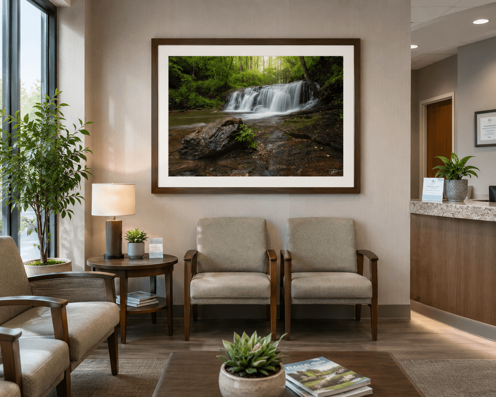 A large, premium framed fine art photograph of a serene waterfall in a lush green forest hanging in a modern medical office waiting room.